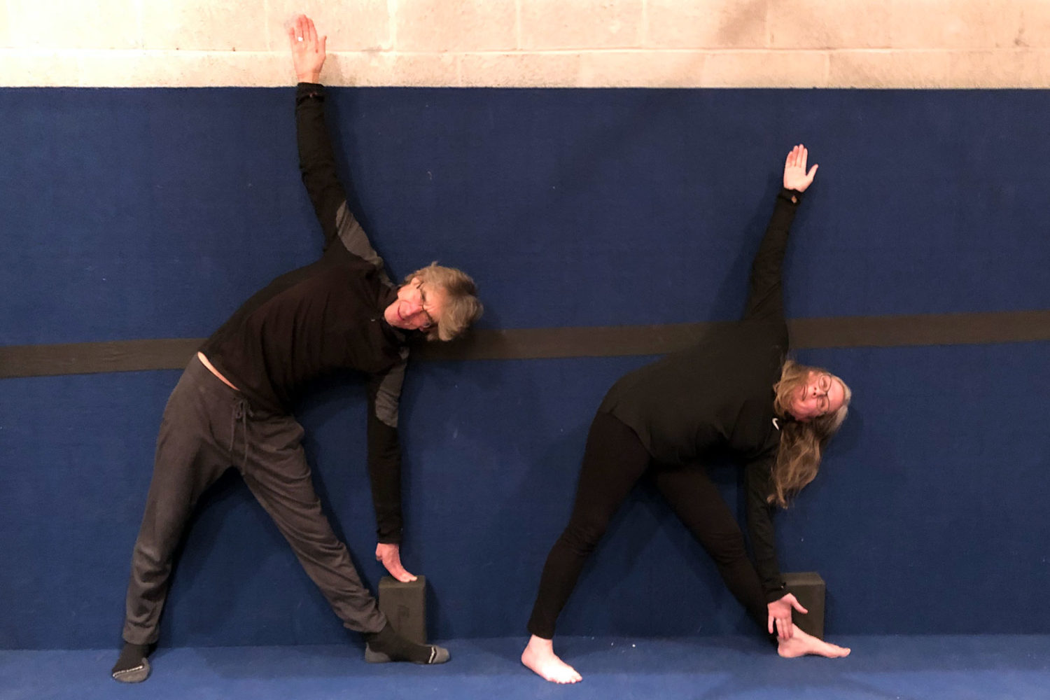 Paul and Peggi doing triangle pose against the wall in yoga class