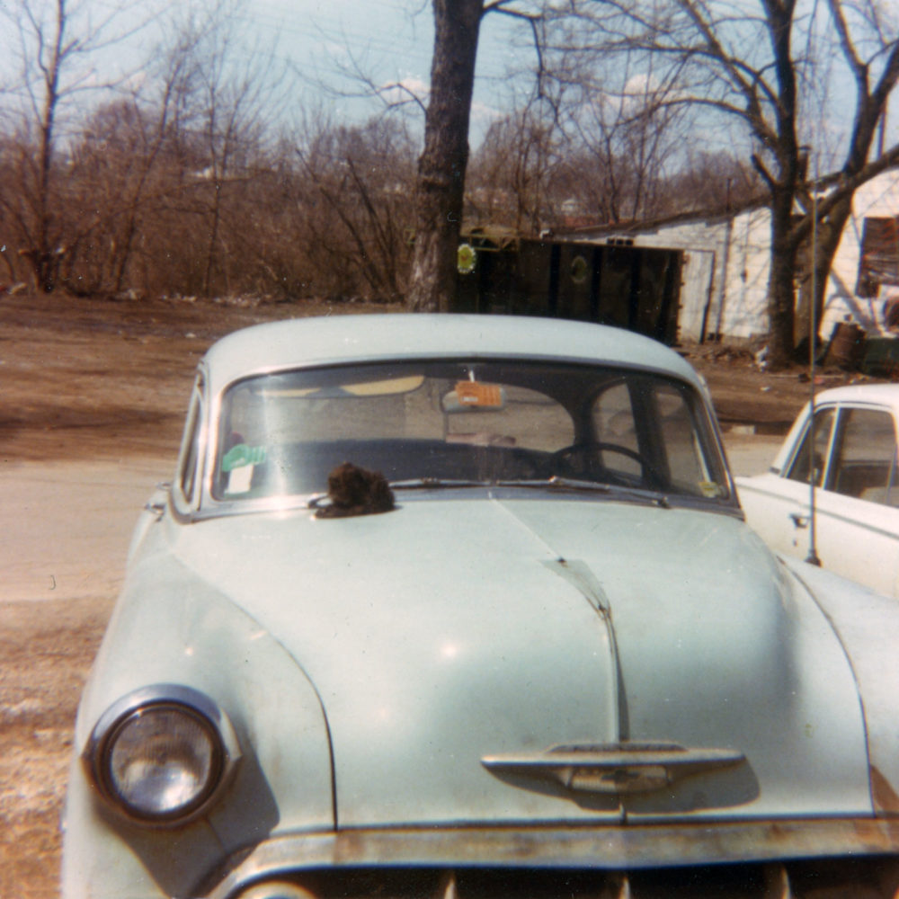 Norm's car in front of the trailer with Scoop on the hood